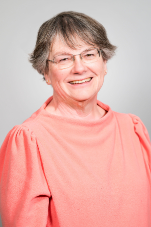 Person with short hair and coral colored shirt smiles at camera