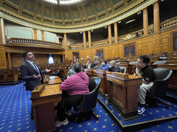 Adults seated in State House chamber listening to Rep. Lewis speak