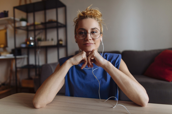 Young adult with light hair in a ponytail wears headphones and smiles at the camera