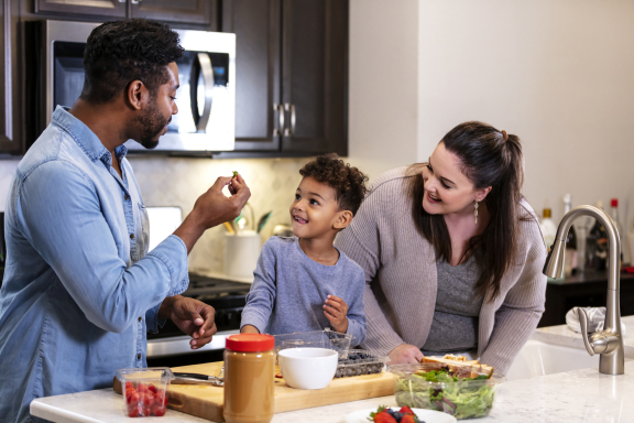 Two adults and a child smile and prepare a snack in the kitchen