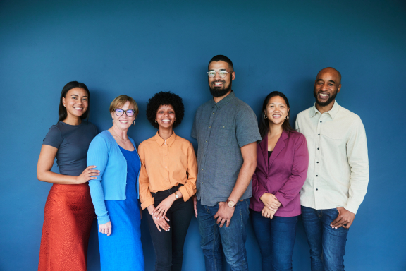 A diverse group of six adults smiles at the camera