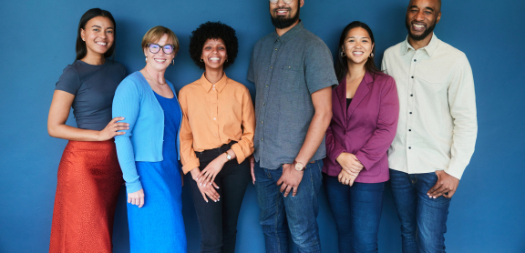A diverse group of six adults smiles at the camera