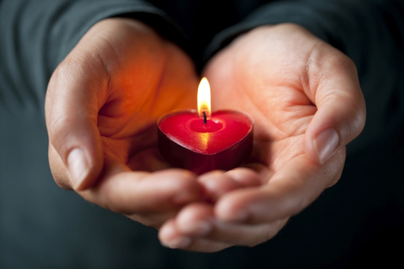 A pair of light brown hands holds a heart-shaped votive candle.