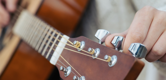 Light-skinned hand tuning an acoustic guitar