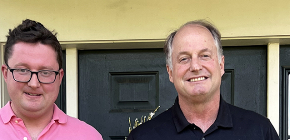 Jack, a young adult man, and his dad smiling in front of their home.