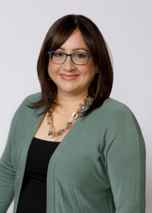 Adult with long dark hair and glasses smiles at the camera