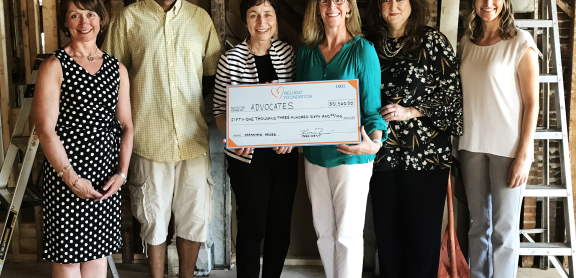 Group of six people standing in a room under renovation; two are holding a large presentation check
