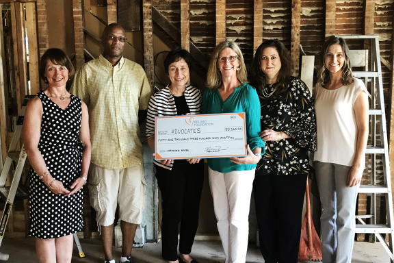 Group of six people standing in a room under renovation; two are holding a large presentation check