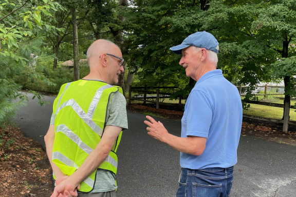 Two older men smiling and walking along a wooded road