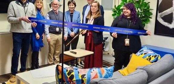 Seven adults in the VAULT space, preparing to cut a blue ceremonial ribbon