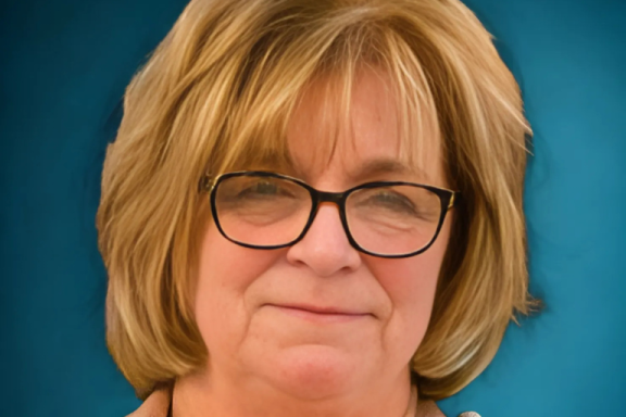 A middle-aged, light skinned woman with honey blond hair and glasses